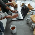Tangan di atas laptop di ruang kerja kreatif dengan model 3D dan prototipe produk sebagai ilustrasi proses pengembangan prototype
